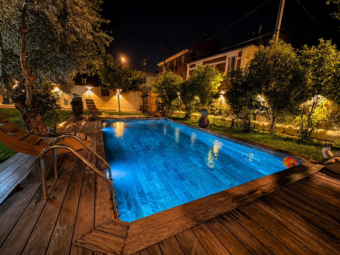 Vue nocturne de la piscine éclairée en bleu, entourée d'un vaste jardin.