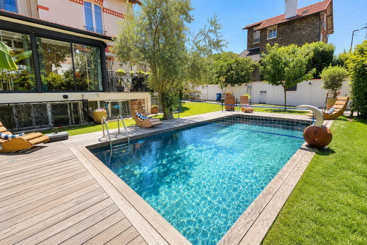 Piscine cristalline avec plage de bois, bordée de verdure et accessible du logis.