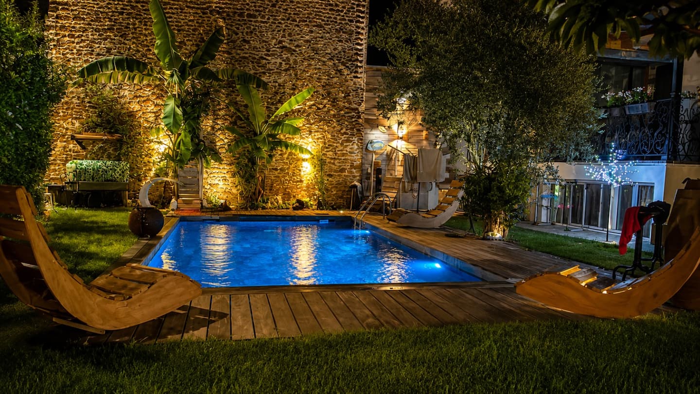 Piscine illuminée le soir avec éclairage architectural et murs en pierre.